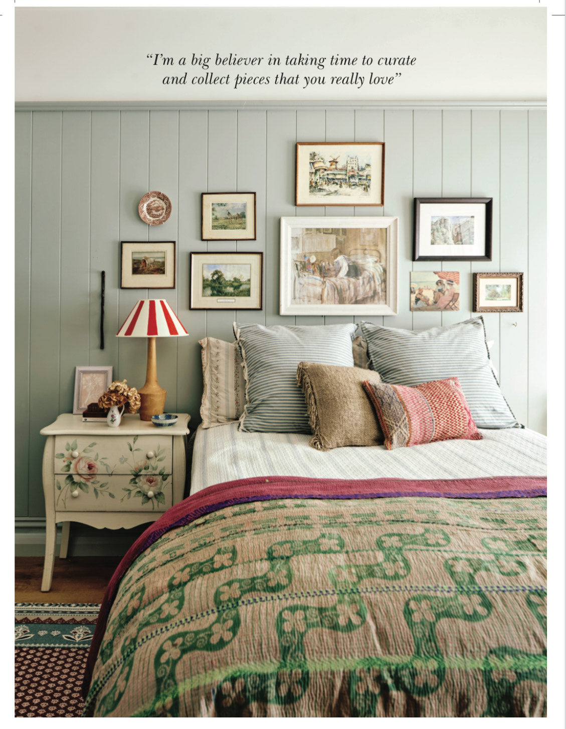 Country style bedroom with eclectic gallery wall over the bed layered with textiles in different patterns, prints and stripes and red striped lampshade.