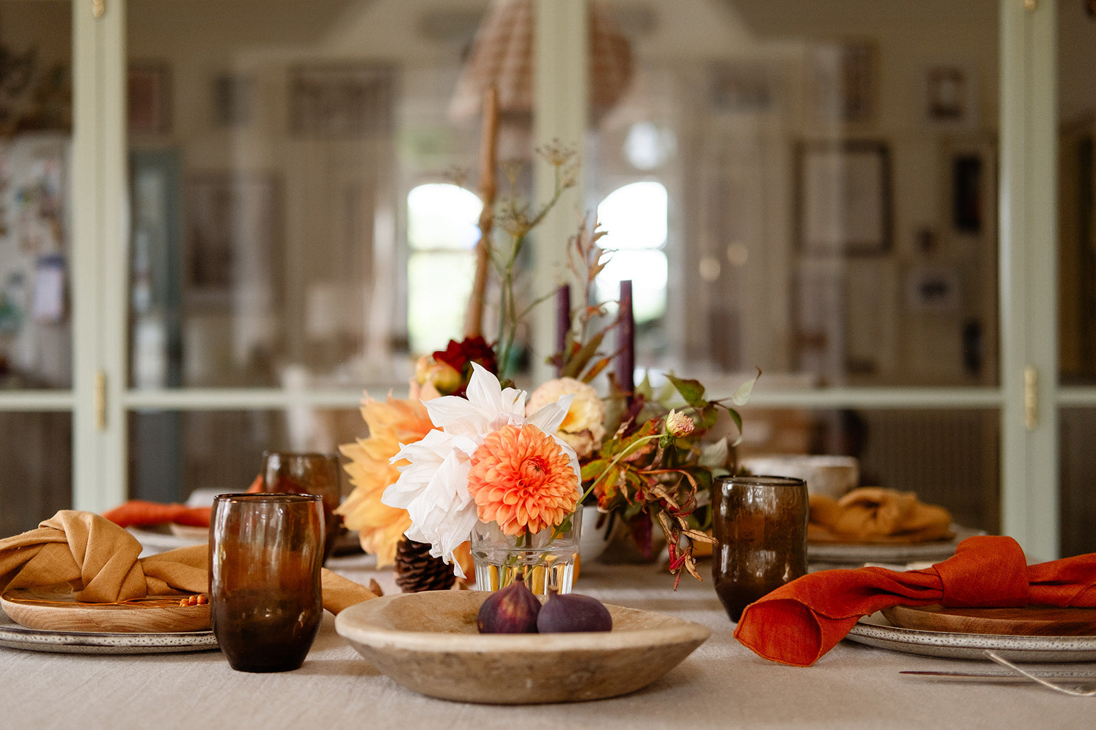 Nature-inspired Table setting with terracotta and tan coloured linen napkins, natural linen tablecloth, vintage marble plate, orange and cream flowers against green crittall style doors