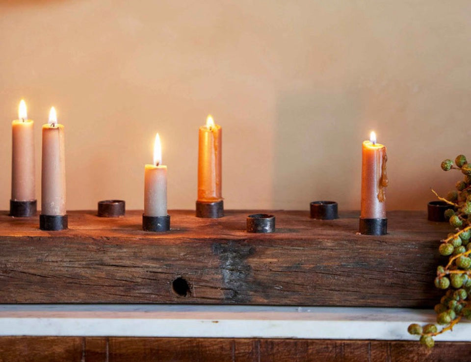 Candles burning in a rustic wooden plank candle holder panel with a woven decorative object above