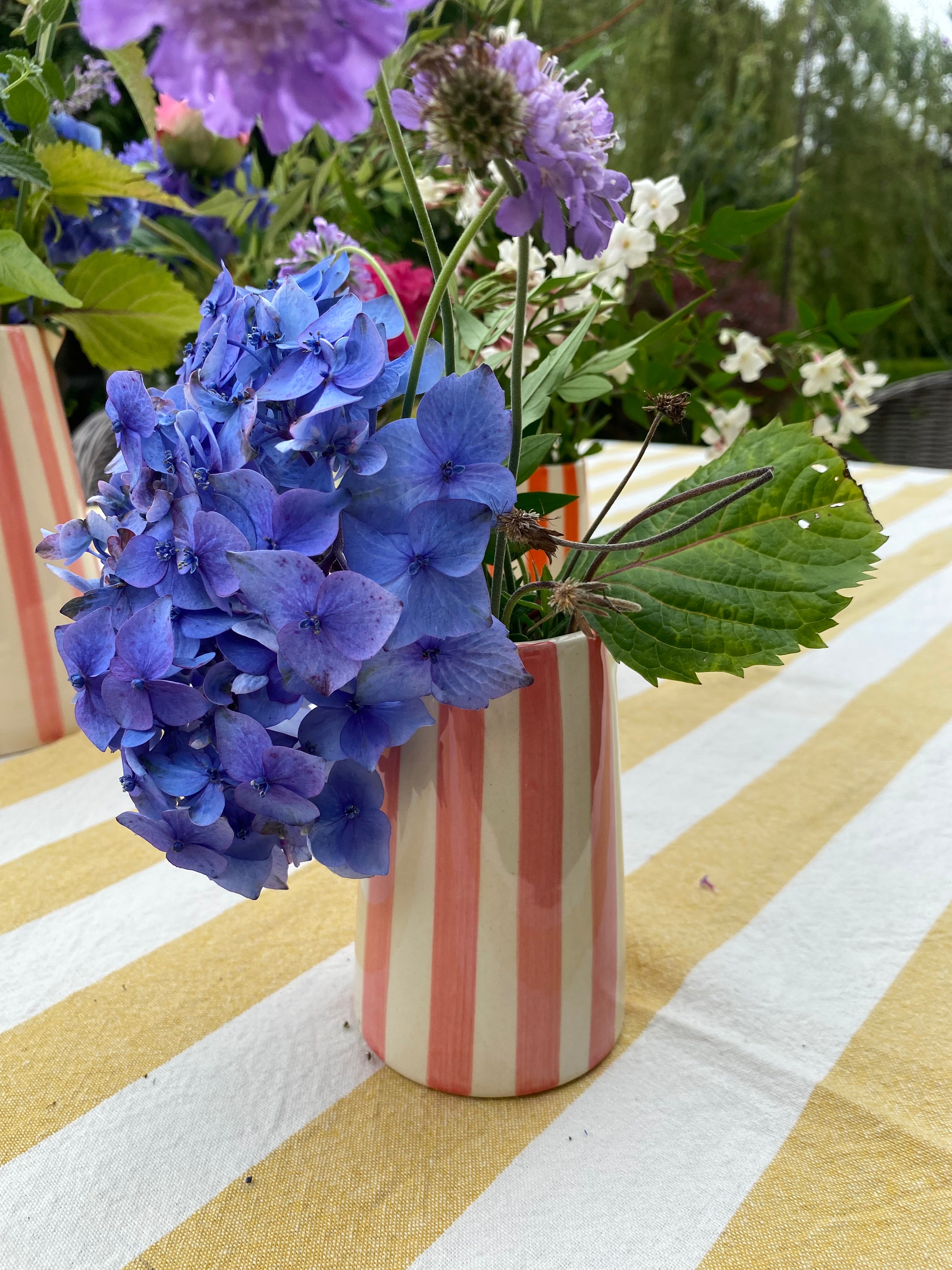 pink striped jug filled with bright flowers on a yellow and white linen tablecloth in an outdoor setting