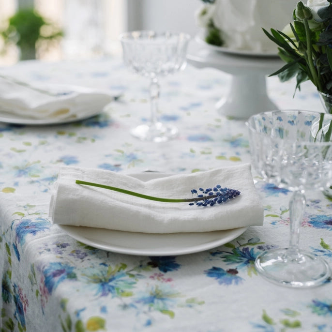 White linen folded napkins with muscari on top on a floral linen tablecloth
