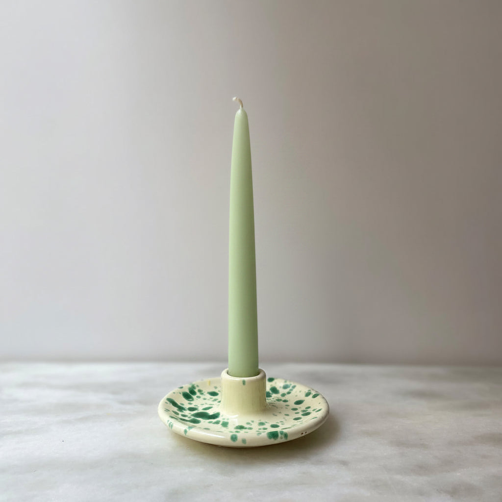 An Italian ceramic green splatter candle holder with a twisted, brown candle placed on a white surface with a plain background.