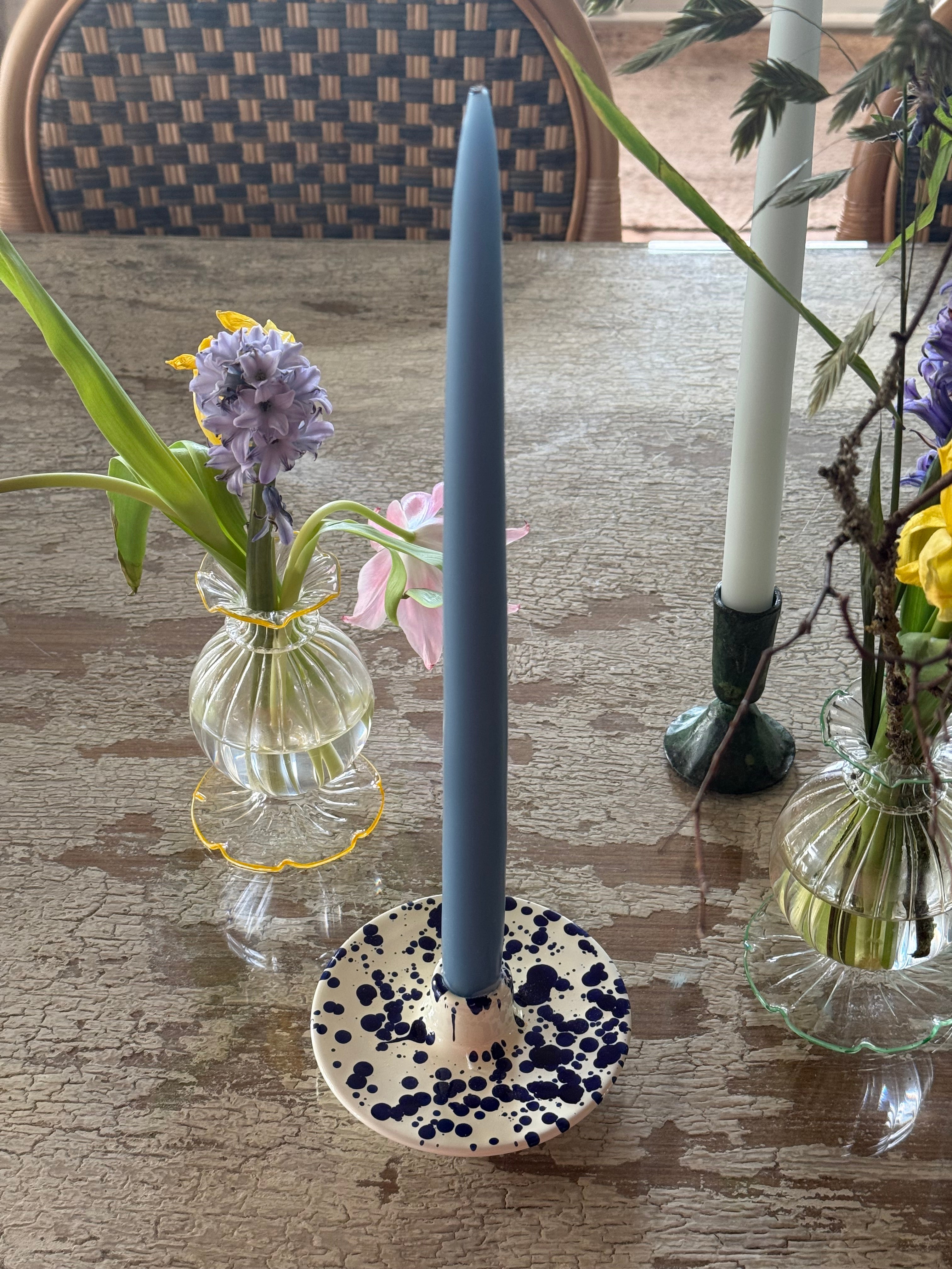 Overhead view of blue splatter ceramic candle holder with blue candle on rustic white wood table with glass frilly vase of hyacinths