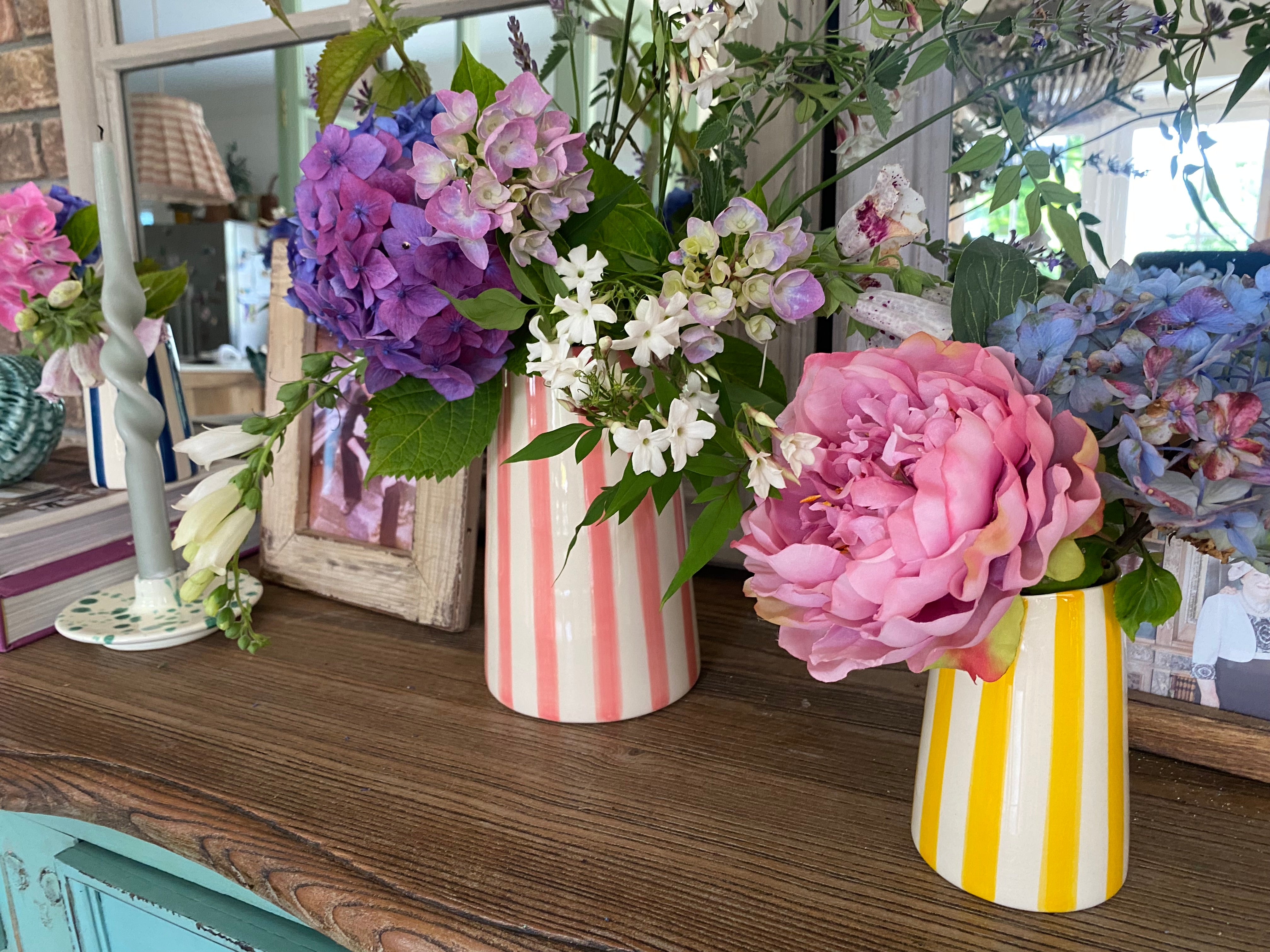 Colourful flowers in striped vases on sideboard with mirror in background