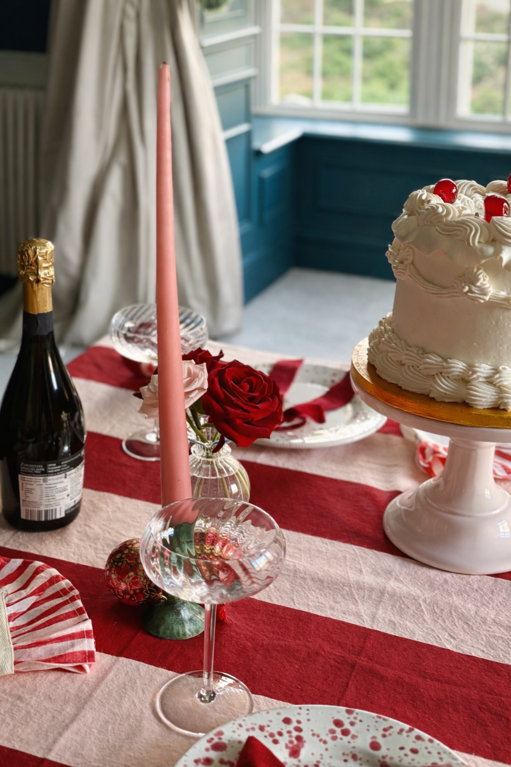 Decorative table setting with red and pink striped tablecloth, lambeth cake, champagne glasses, pink tapered candles