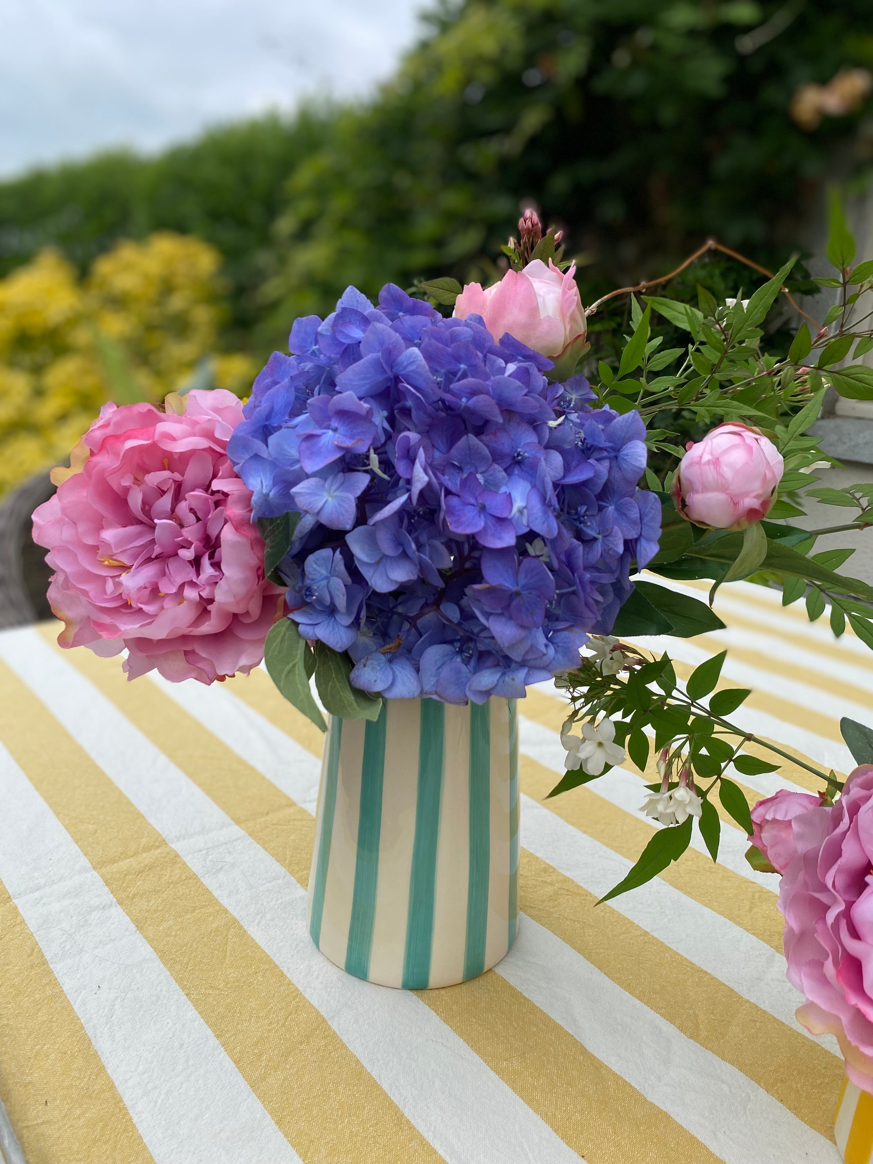 Mint striped pitcher filled with blue and pink flowers in an outdoor setting