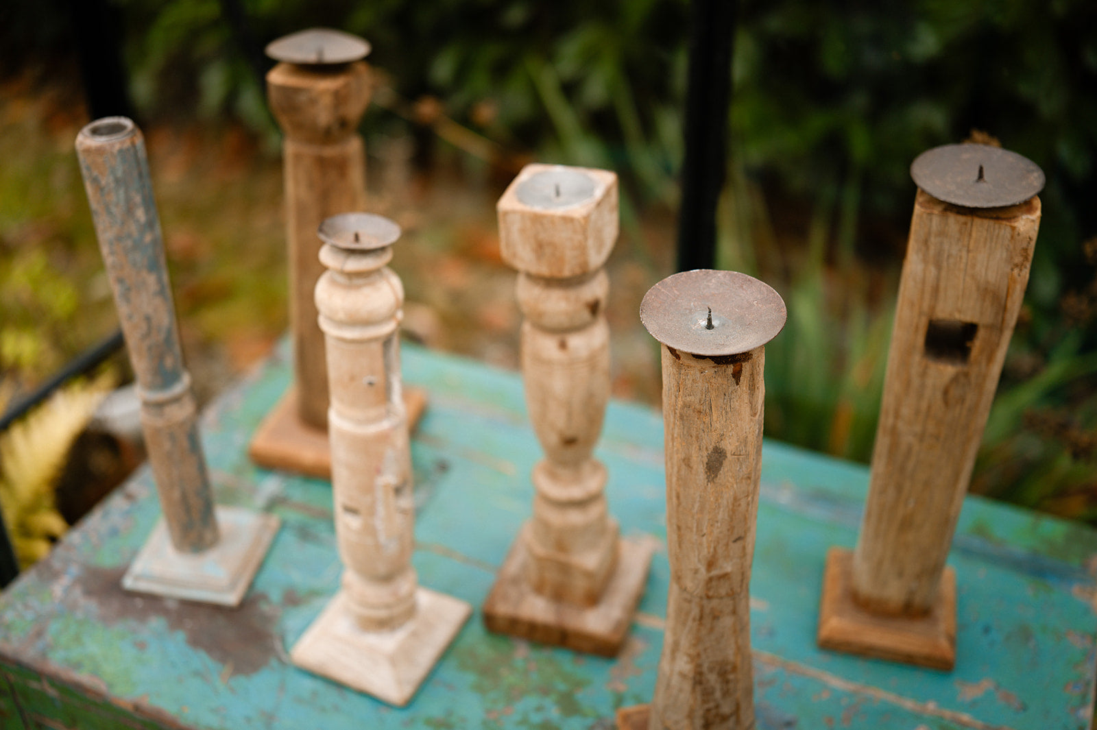 Set of rustic wooden candle holders on a textured surface with blurred greenery in the background.