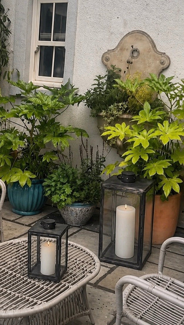 Stone patio area with terracotta and turquoise pots of green plants with grey outdoor furniture and black lanterns
