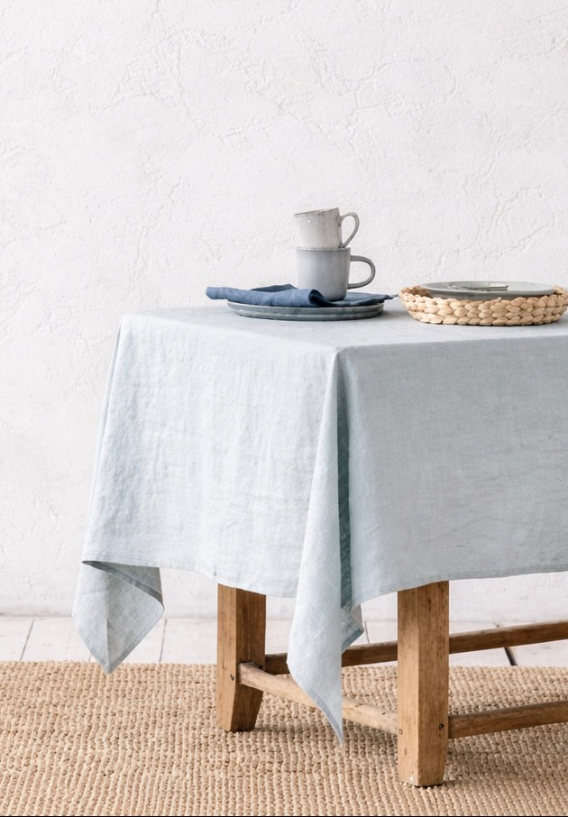 Close up shot of a duck egg blue tablecloth draped over old wood table against textured white wall.