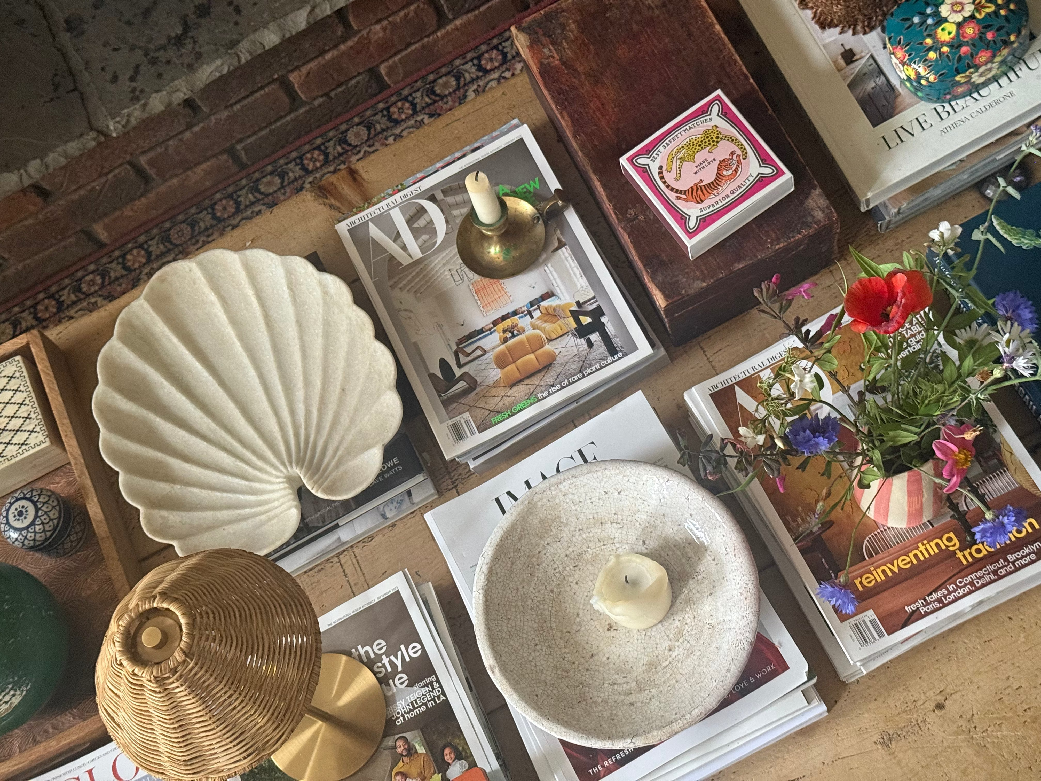 Overhead view of coffee tablescape with cordless rattan lamp, marble shell platter, striped jug of flowers, books, magazines and other decorative elements
