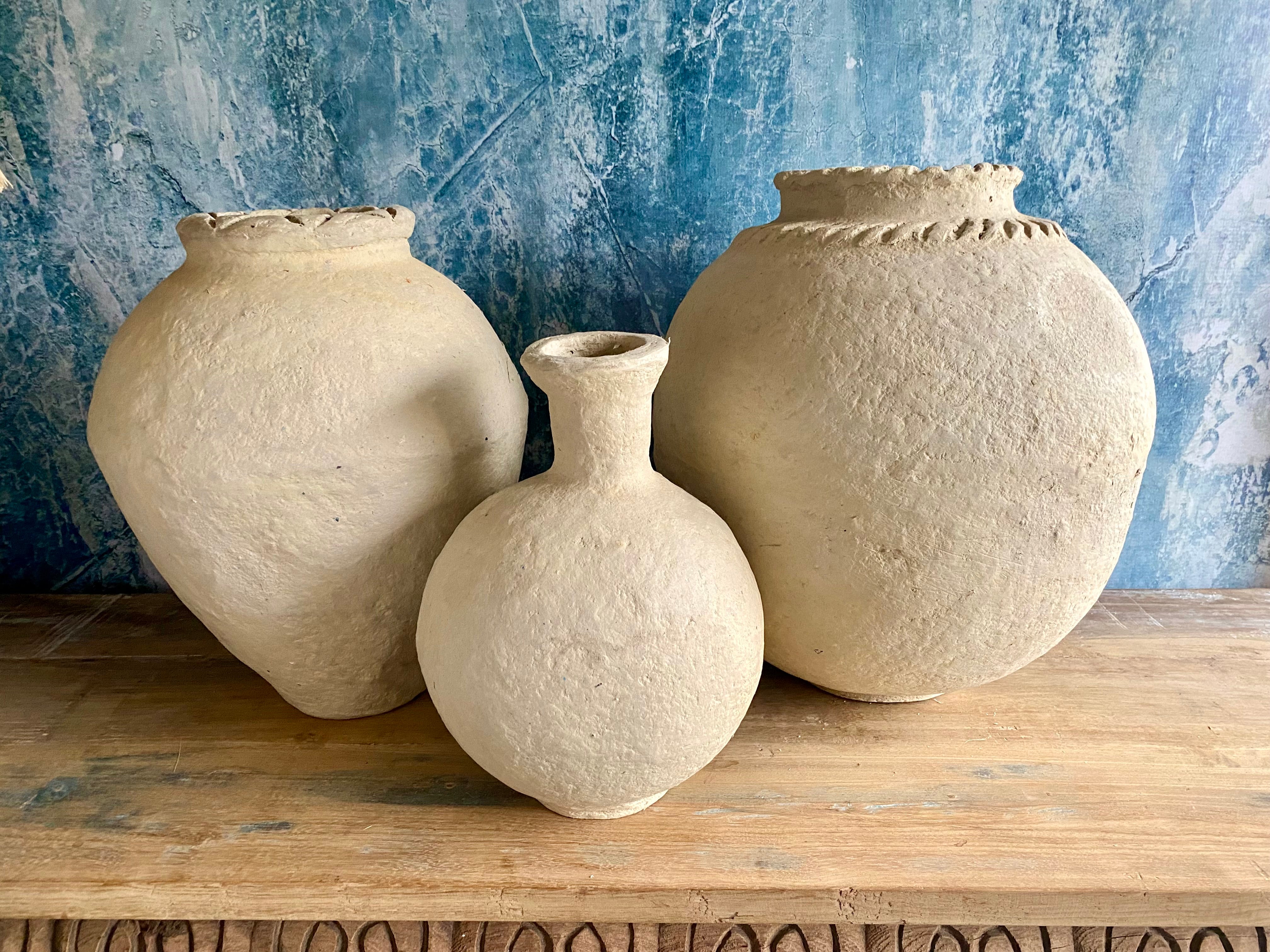 Three papie- mache pots of varying sizes on a wooden surface with a textured blue wall background.