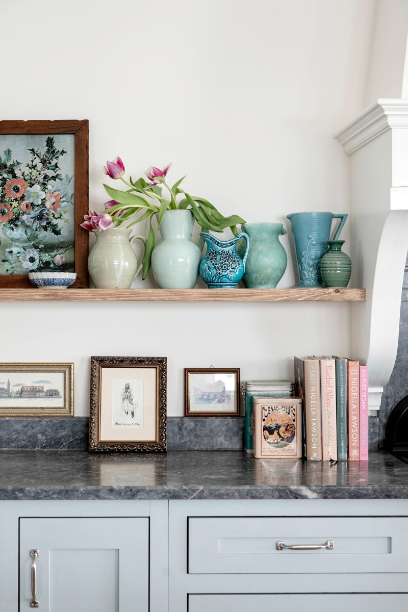 Decorative shelf with vases, books, and framed pictures in a kitchen setting.
