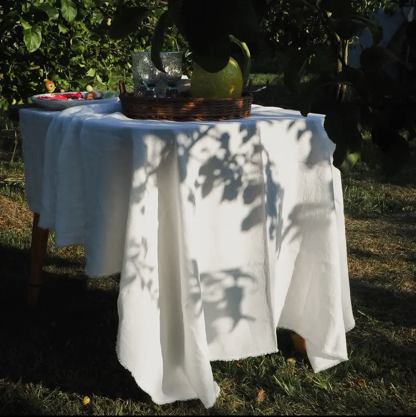 Stonewashed white 100% linen tablecloth with fringes draped pver a table in a garden setting from Irish online homewares shop Amber + Willow