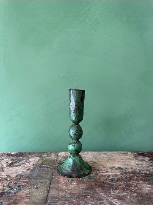 Close up shot of verdigris candleholder on rustic wood surface against green background