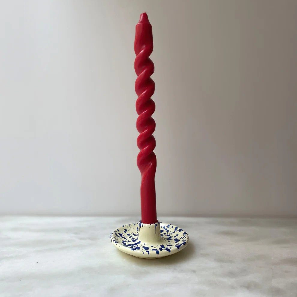 Red twisted candle on a decorative candle holder against a plain background