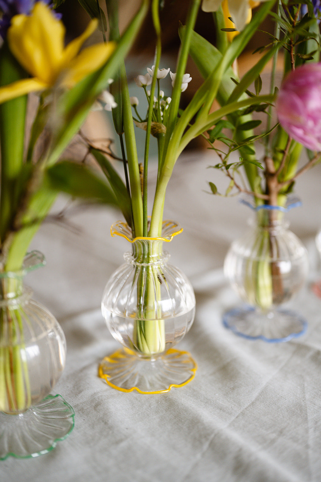 Small glass vases with yellow and pink flowers on a textured surface