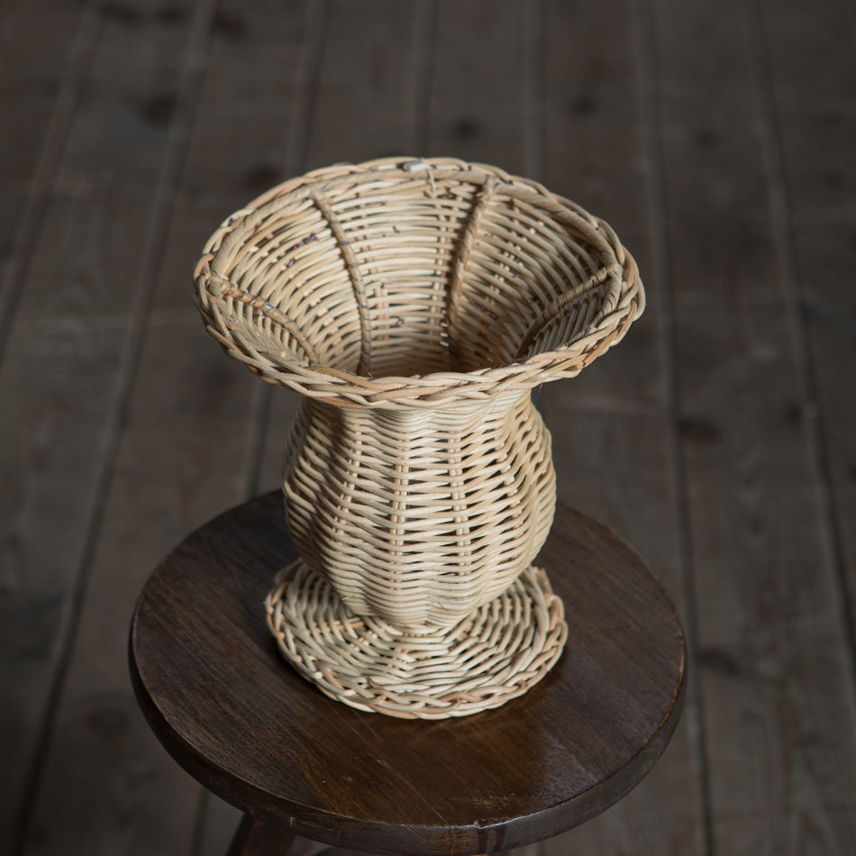 Rattan urn on a wooden stool with a dark wooden floor background