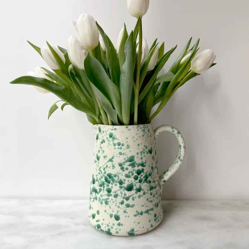 A ceramic splatter jug with a green and white speckled pattern, containing a bunch of white tulips.