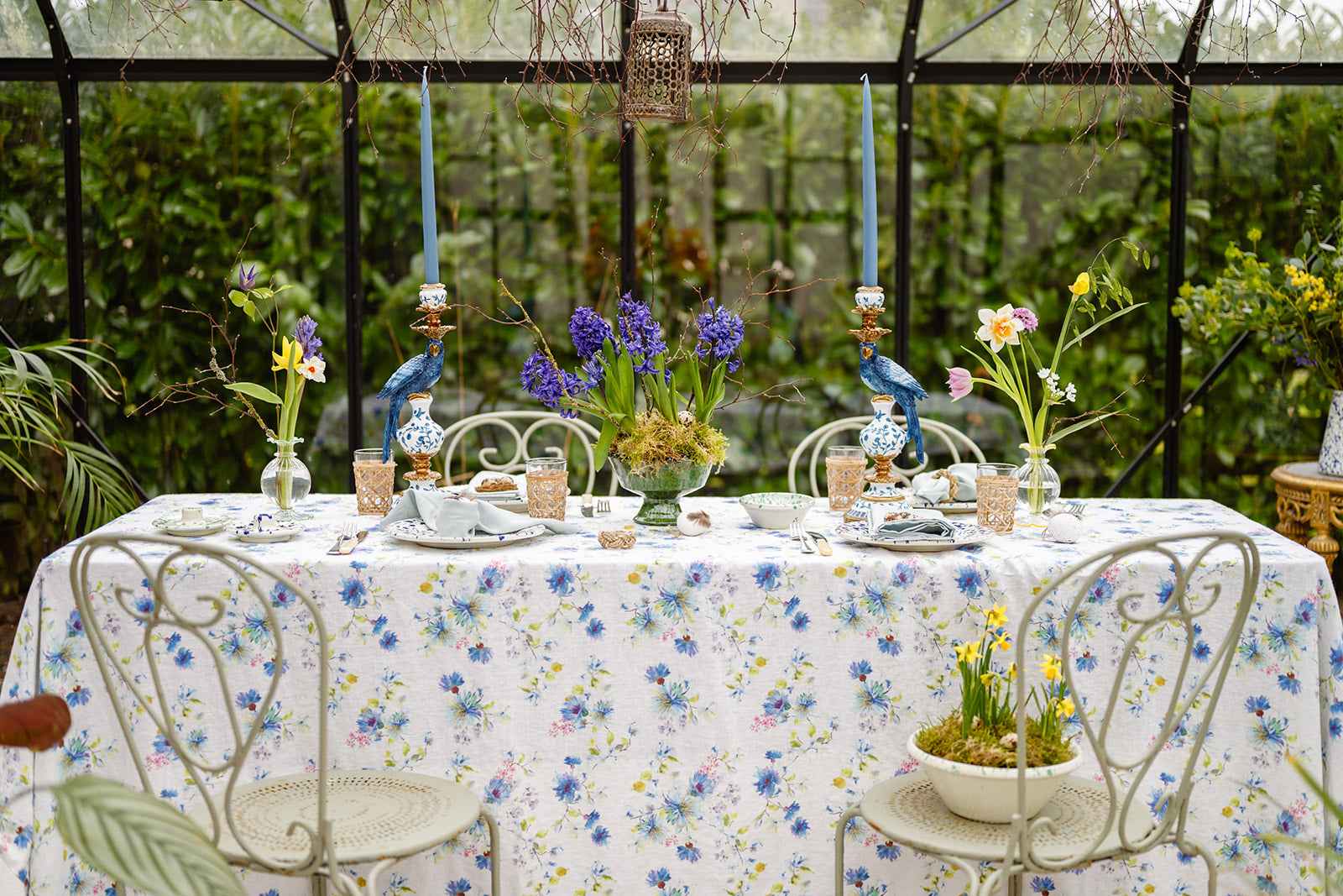 Decorative table setting with floral tablecloth and centerpieces in a greenhouse.