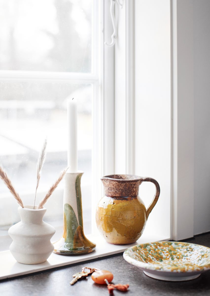 Rustic terracotta jug with ochre glaze at the bottom on a window sill next to other handpainted ceramics