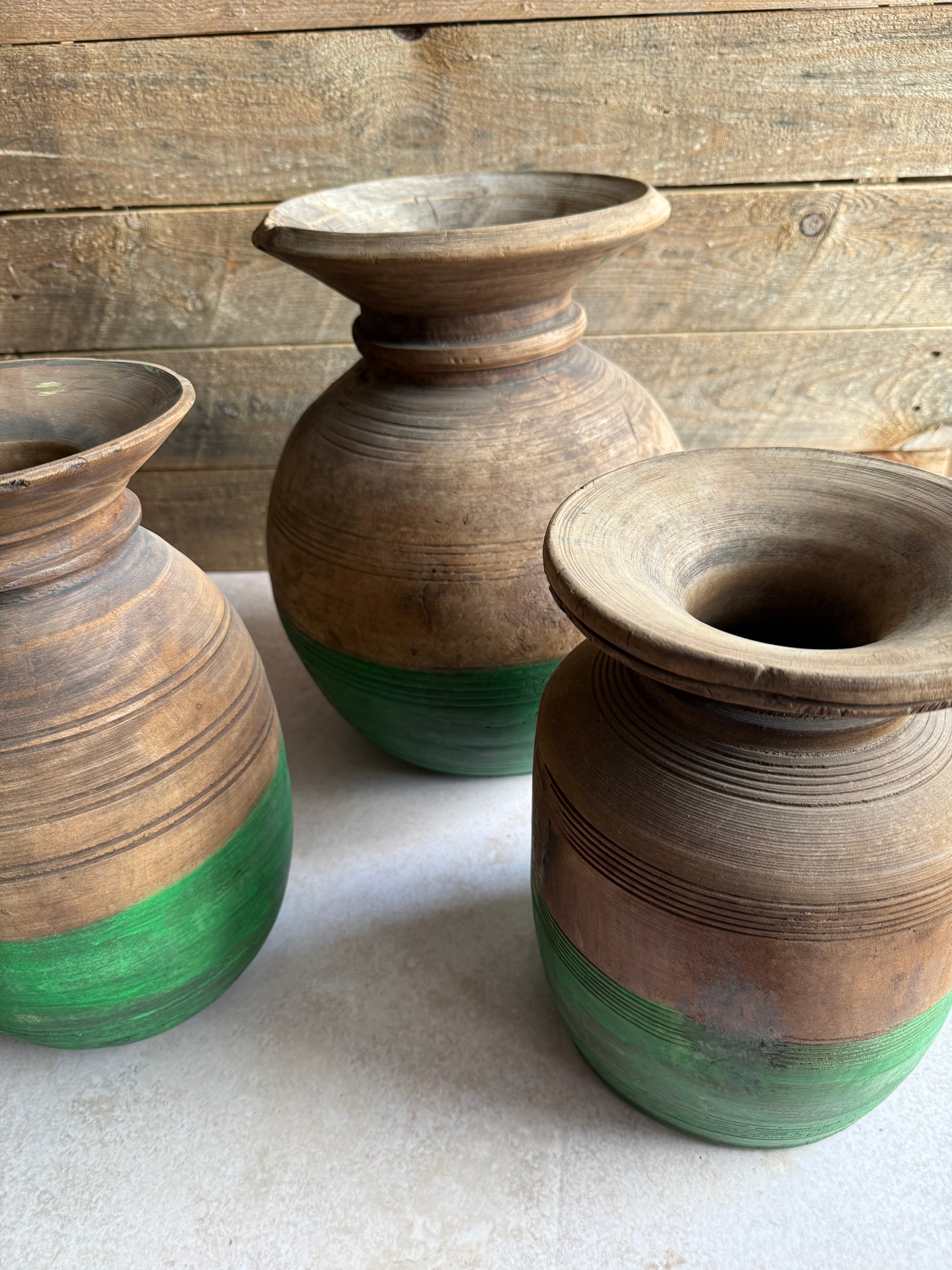 Two wooden vases with green accents leaning against a wooden and white wall.