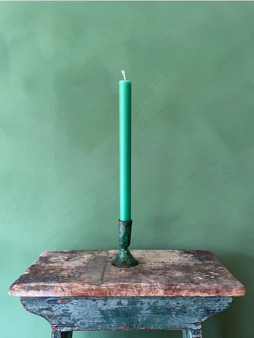 Small verdigris candleholder sitting on a rustic table against a turquoise background
