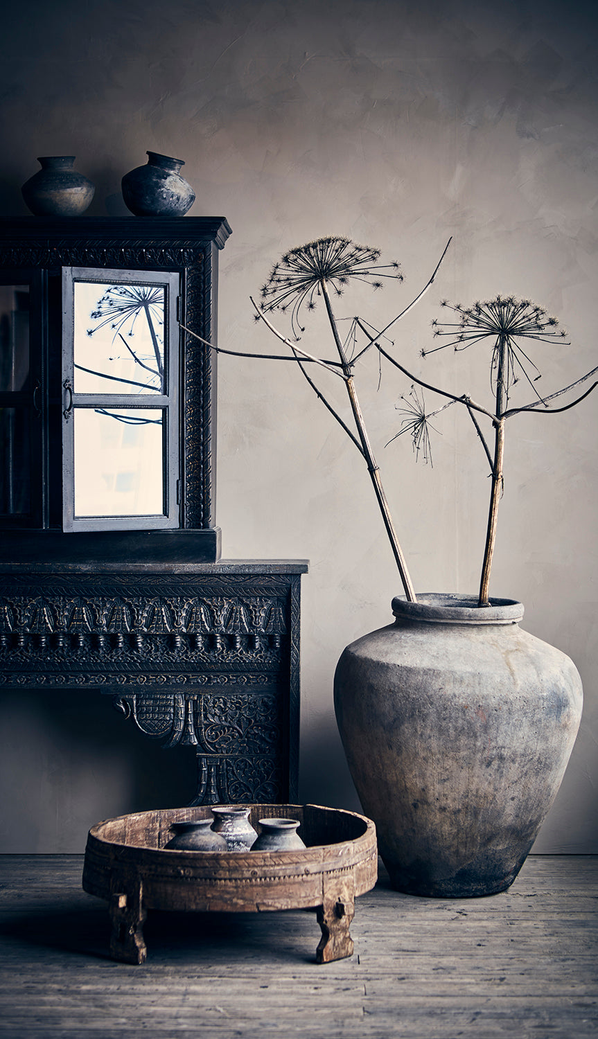 Decorative interior scene with a large vase, small table, and framed mirror.