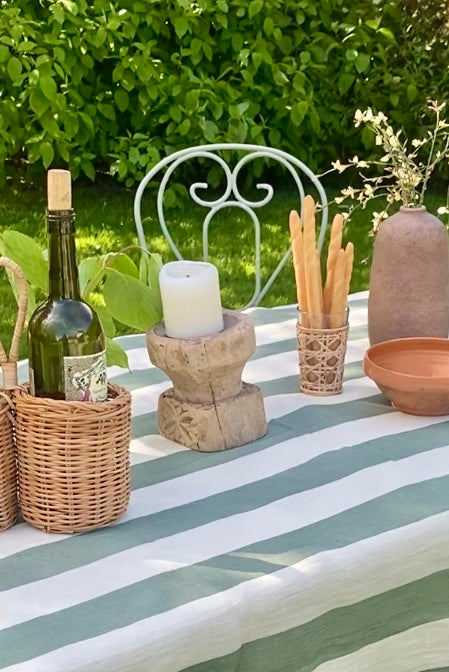 Outdoor tables setting with green and white striped tablecloth, antique carved wood seeder, rattan bottle holder, terracotta vase