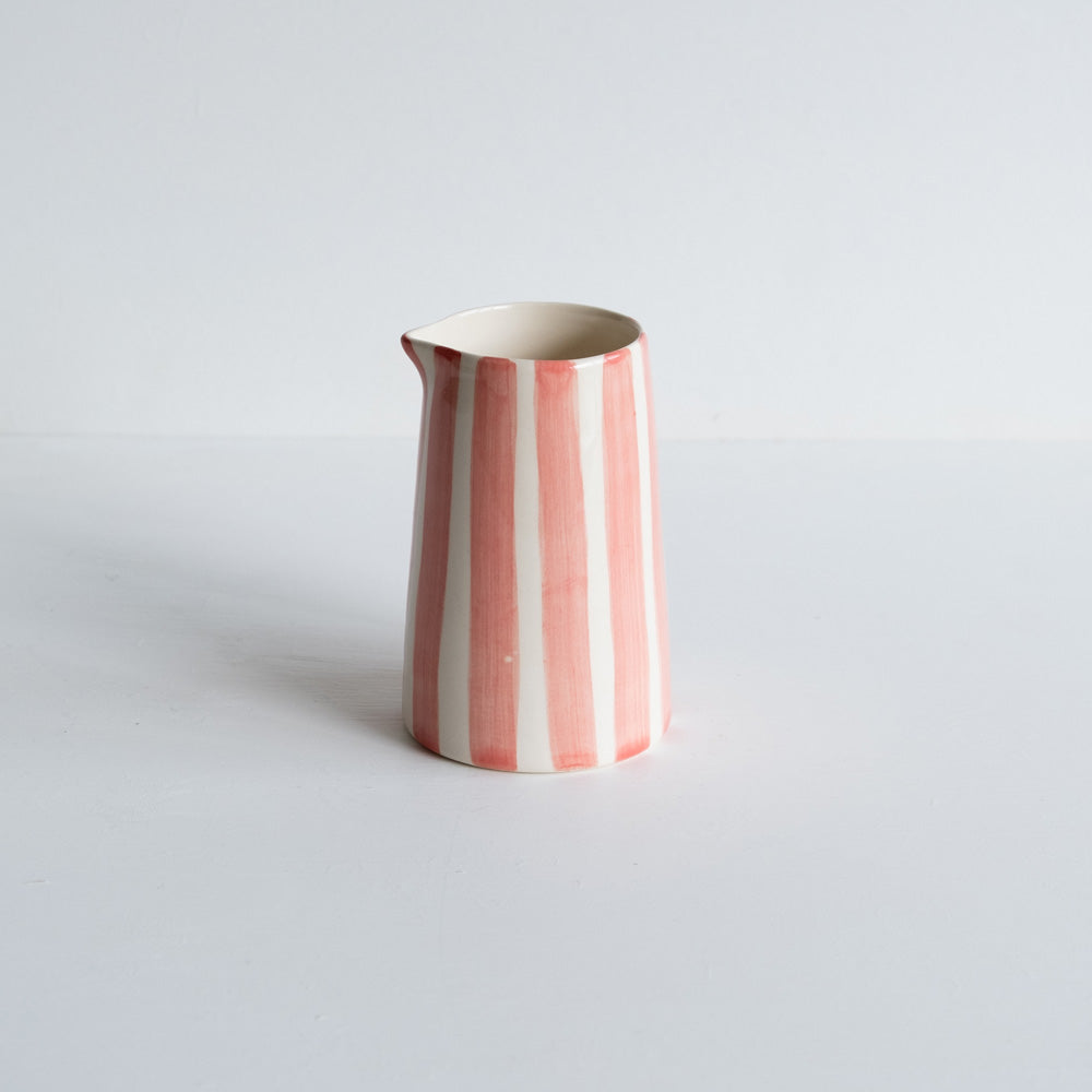 A handmade ceramic jug with pink stripes on a white background.