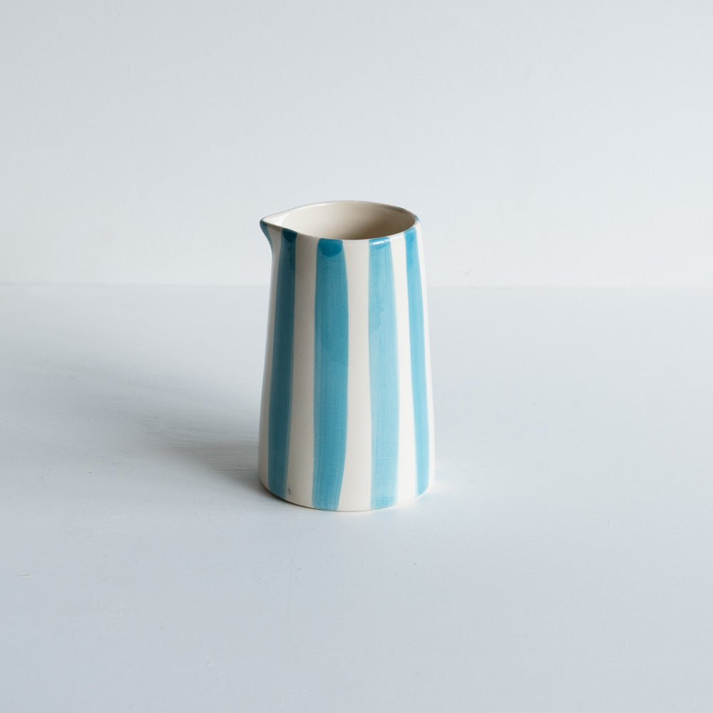 A ceramic jug with turquoise and white stripes on a plain background.