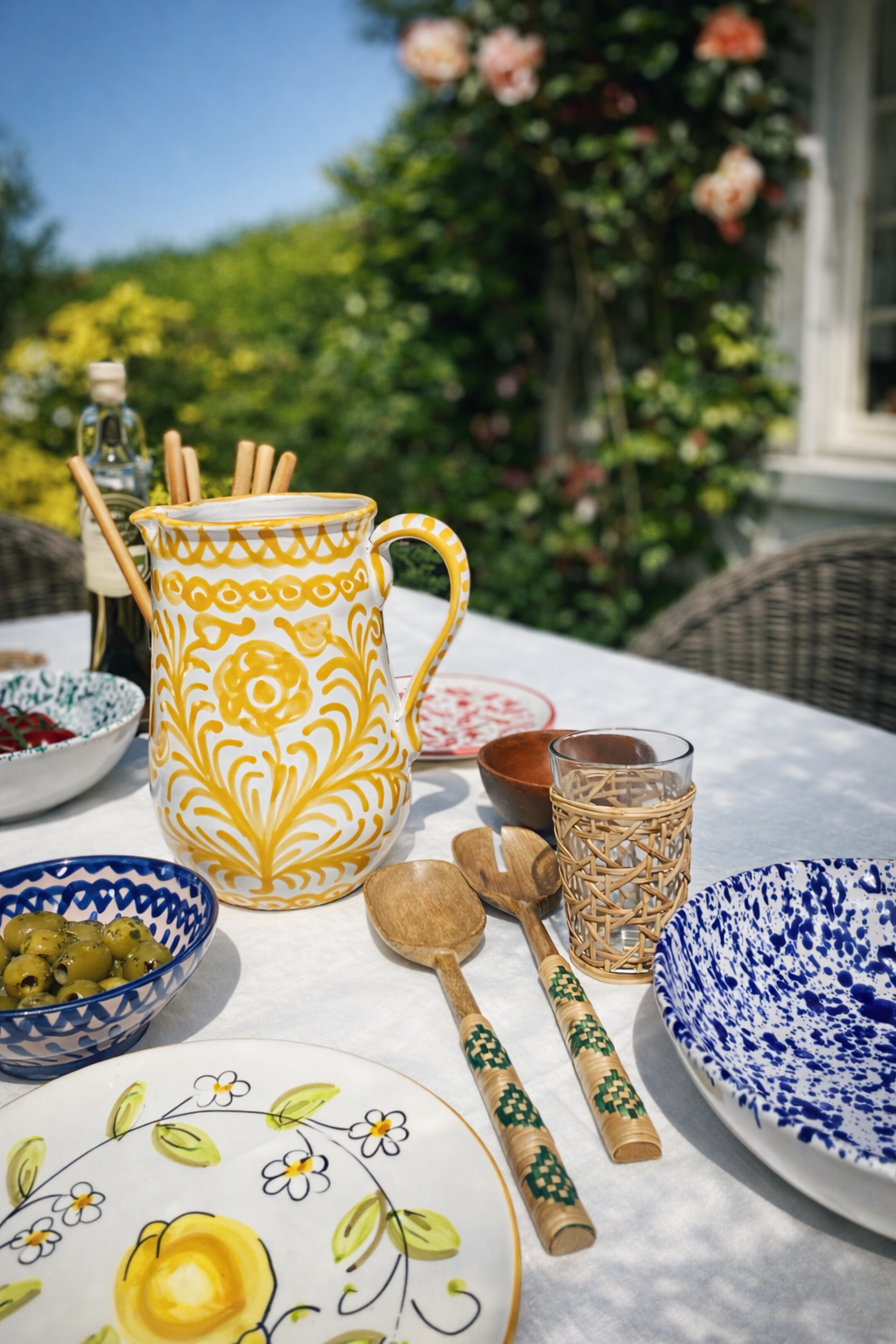 Outdoor table setting with decorative ceramic pitcher, plates, and bamboo salad servers
