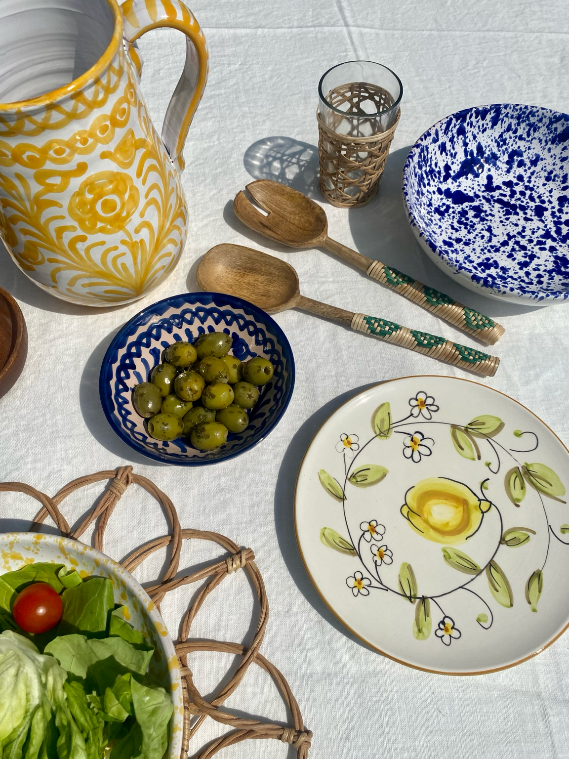Dining table setting with ceramic dishes, a pitcher, and bamboo salad servers