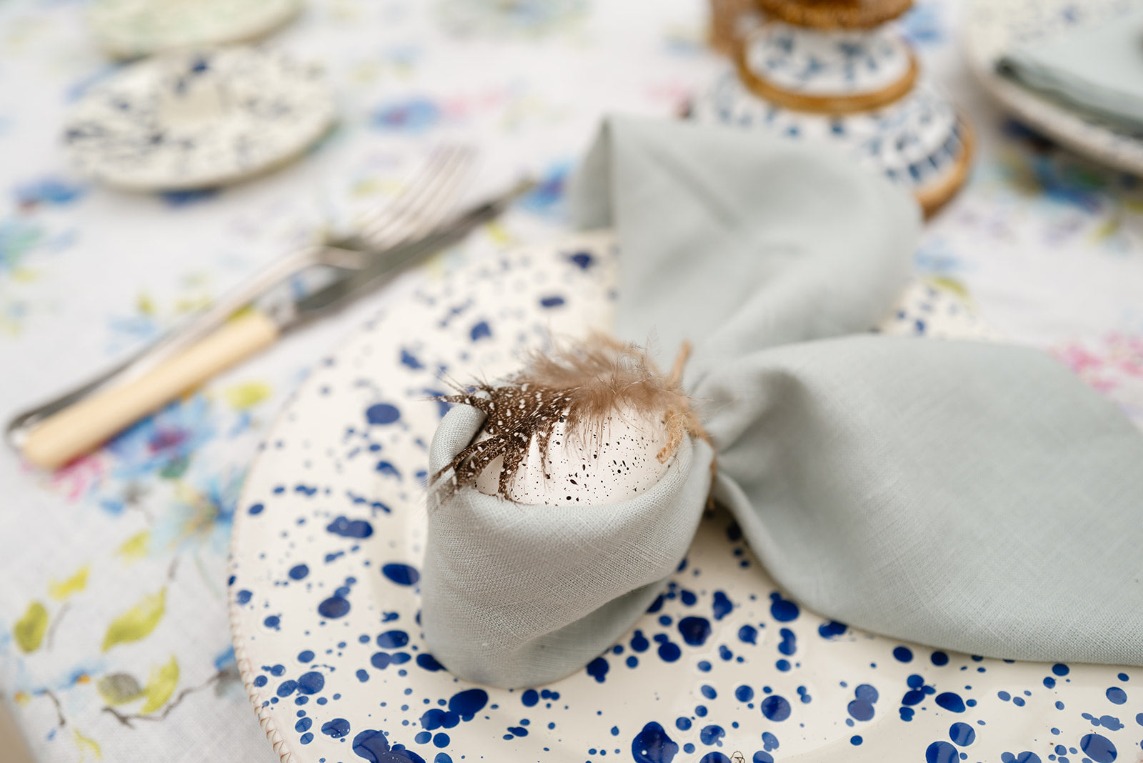 Close up of duck egg blue napkin tied into bunny ears with decorate white egg and feather on blue splatter plate