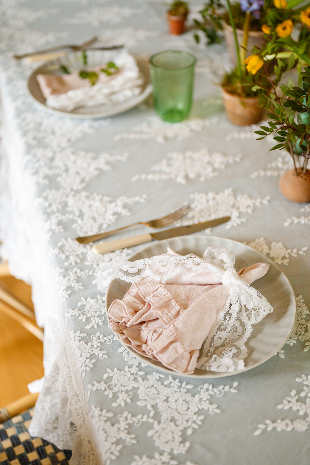 Image of table setting with lace tablecloth draped over duck egg blue linen tablecloth with ruffled napkins an flowers
