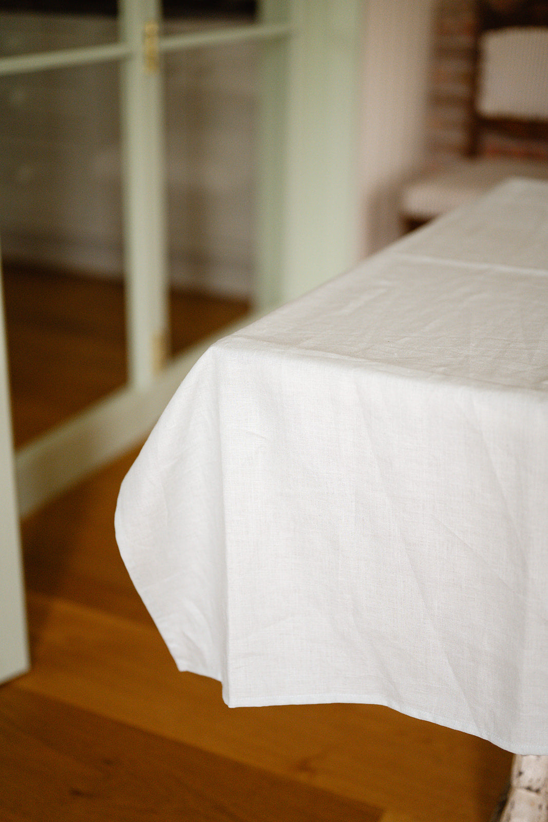 Close up shot of a duck egg blue tablecloth draped at corner of table with green crittall doors in the background