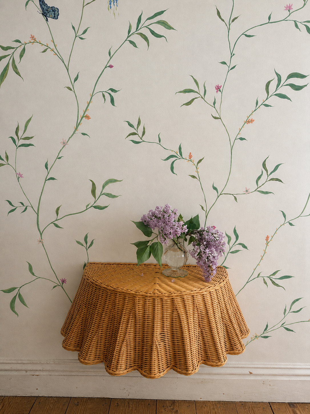 Floating rattan skirted console table with vase of fresh lilac against a hand painted botanical wall mural