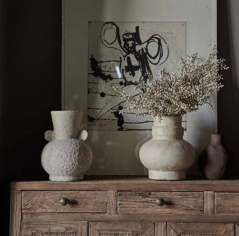 Two creamy beige textured vases on rustic wood sideboard in front of abstract art