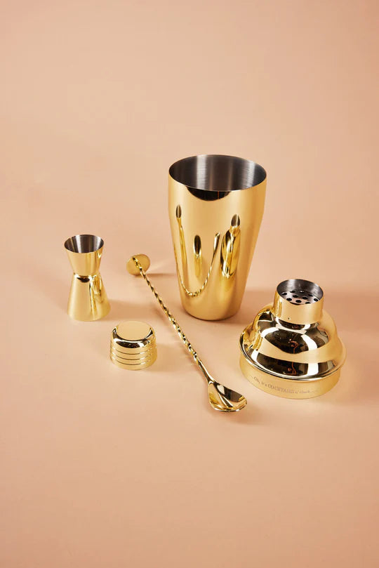 Gold-plated cocktail shaker , jigger and spoon on peach background