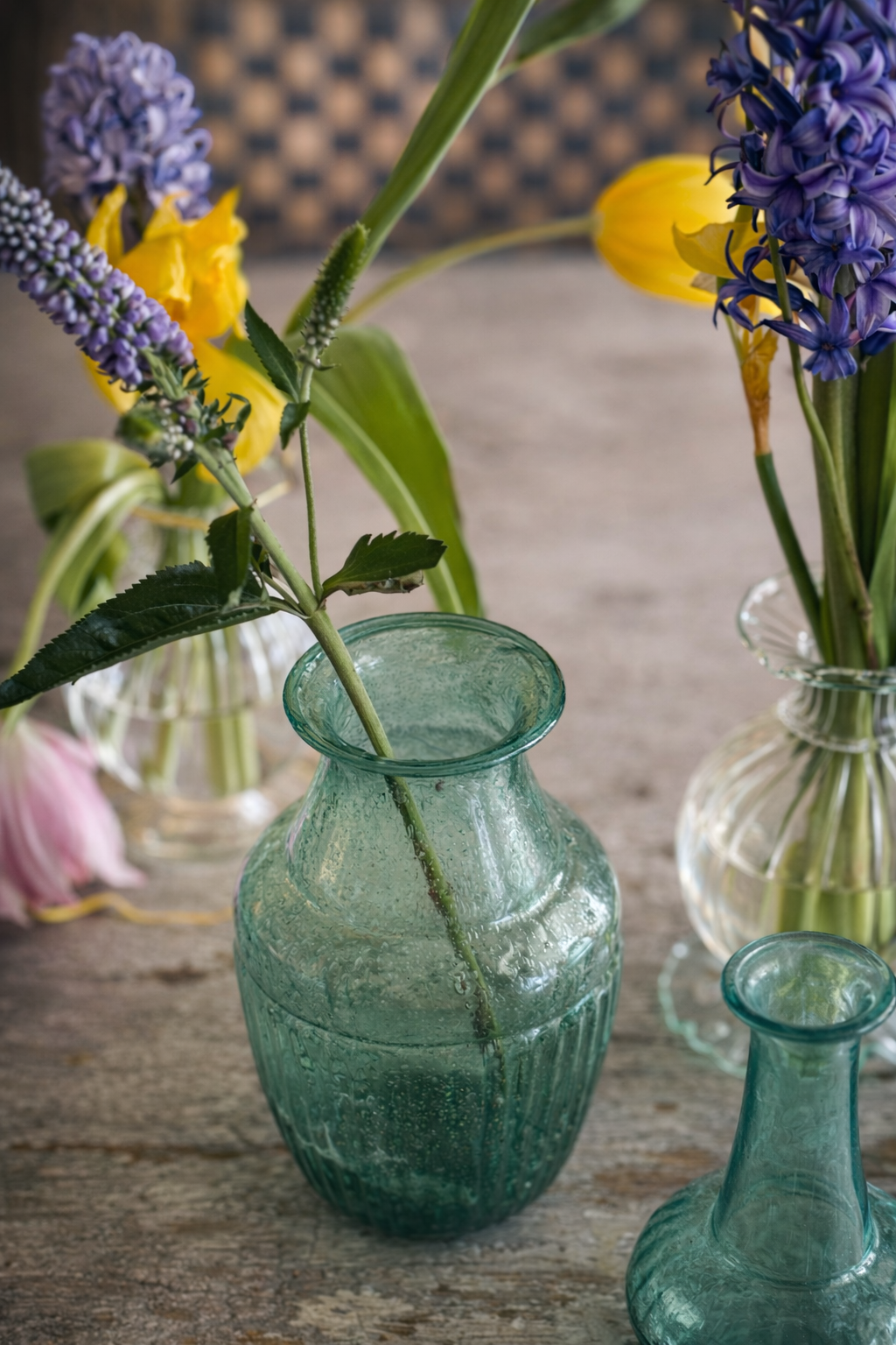 Green glass vase with flowers on a wooden surface