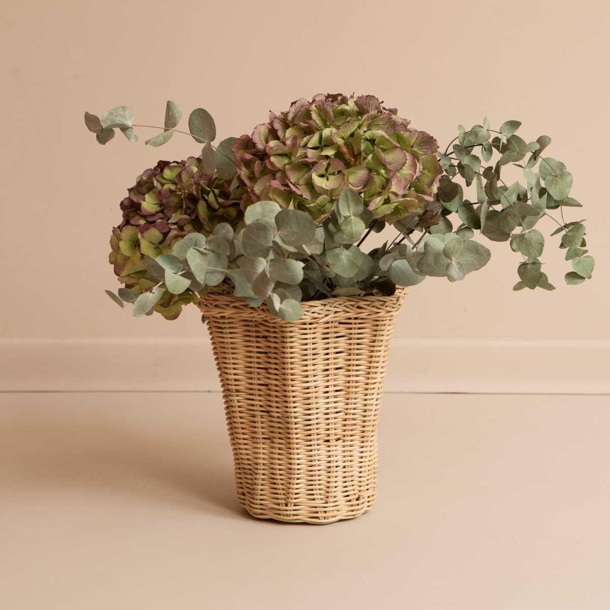 Wavy rattan vase with flowers on beige background