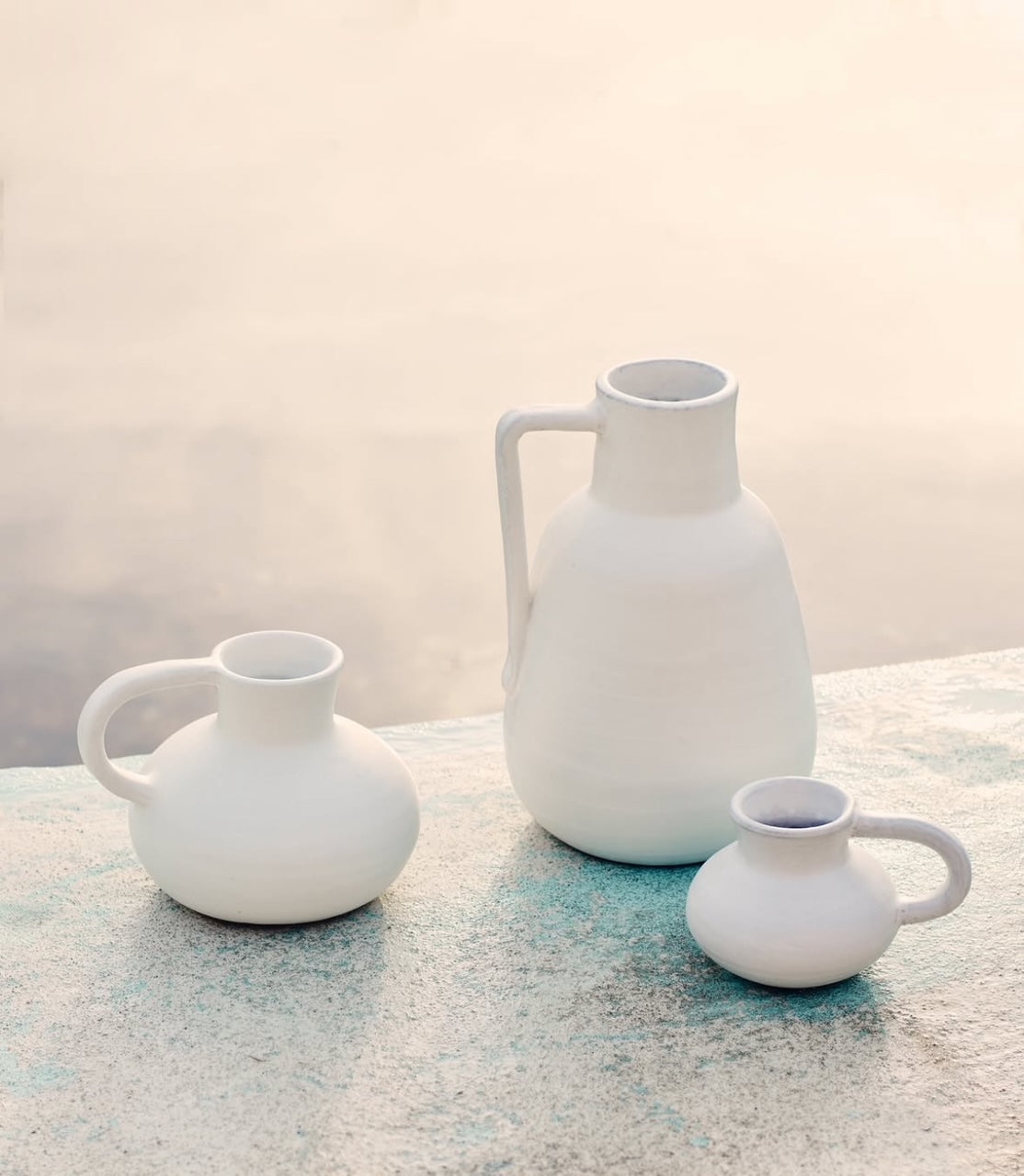 Three white ceramic pitchers on a textured surface with a light background