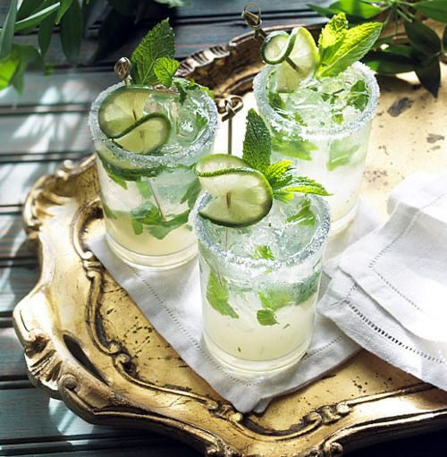 Three glasses of mojito with lime and mint leaves on a gold tray.