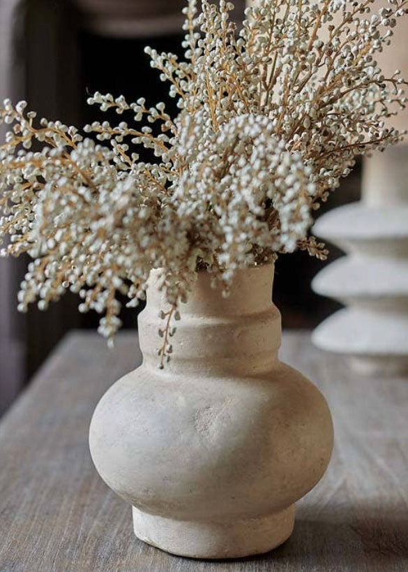 A cream papier-mâché vase with a floral arrangement on a wood console sideboard.