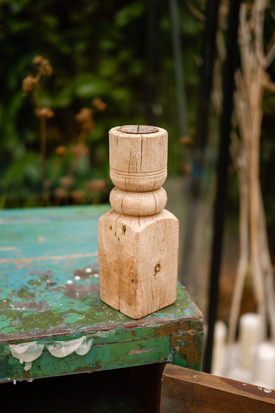 Wooden candle holder on a rustic green table with blurred natural background