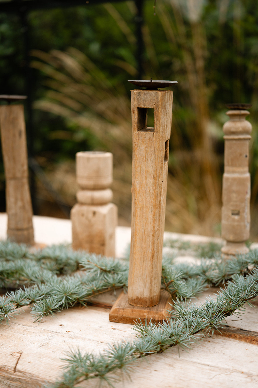 Wooden candle holders on a rustic wooden surface with greenery