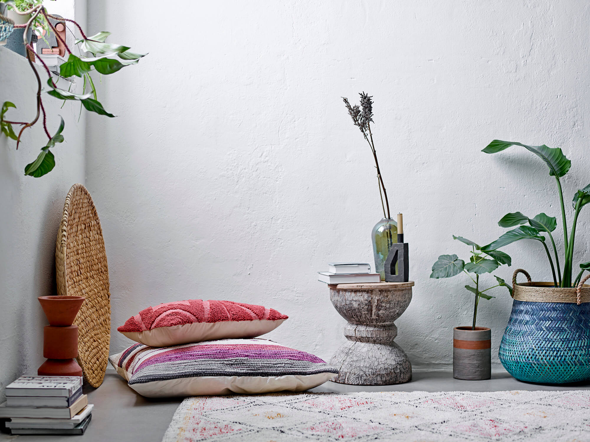 Bohemian style room with white washed walls, rustic reclaimed wood stool, large floor pillow, woven wall plate, large turquoise basket with plant