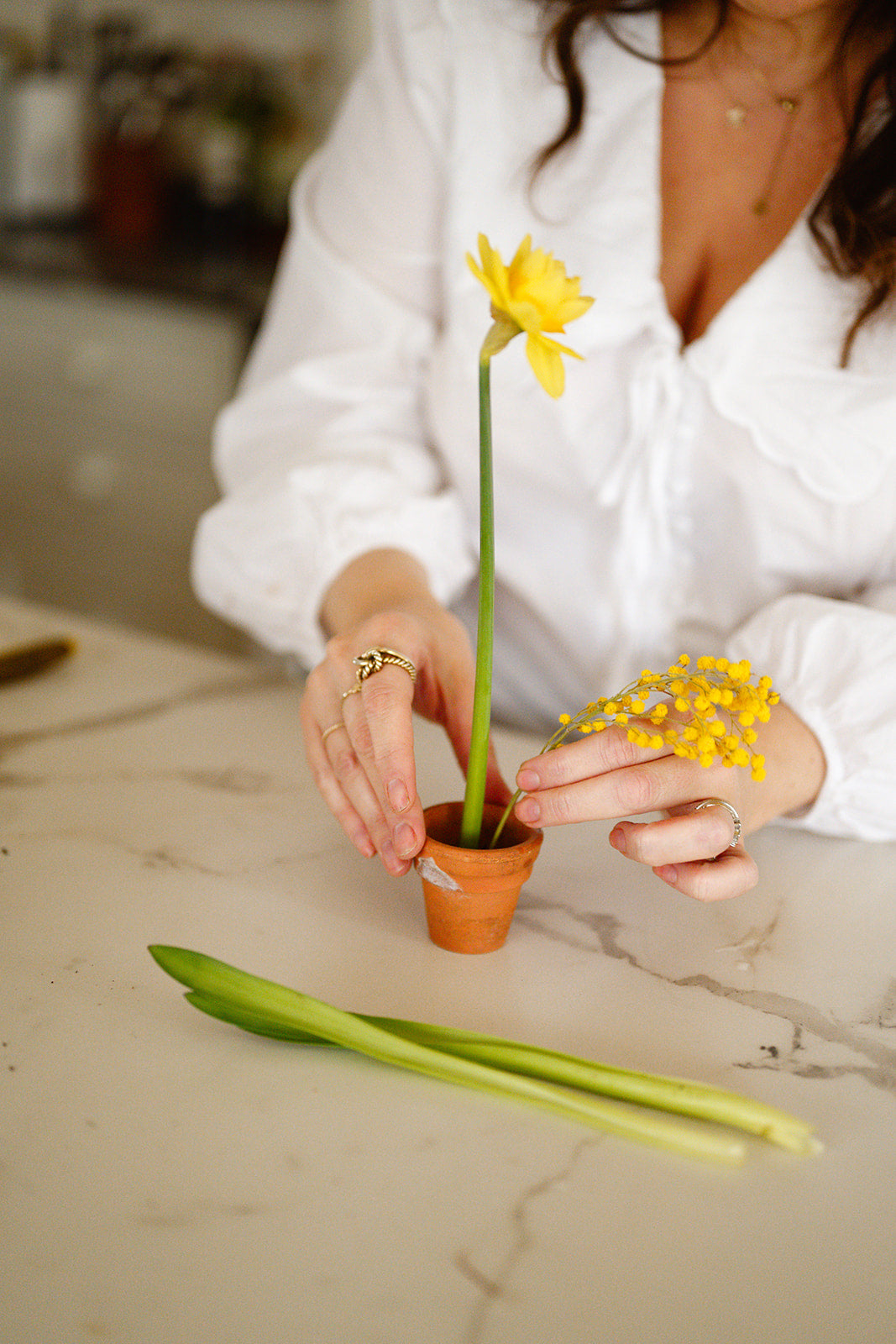 woman arranging spring flowers in small terracotta pot using metal flower frog