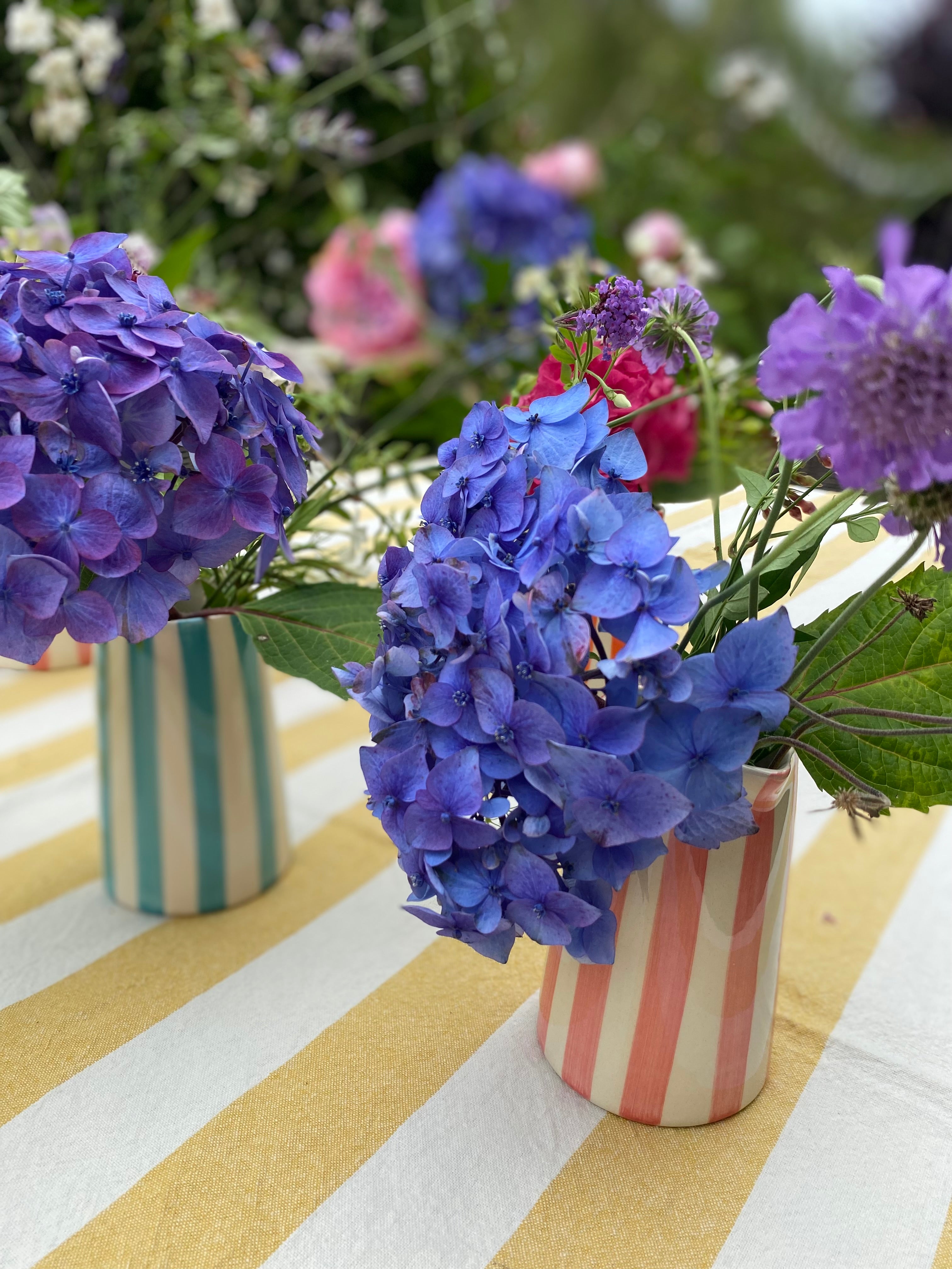 Striped ceramic jugs with bright coloured flowers on yellow striped tablecloth