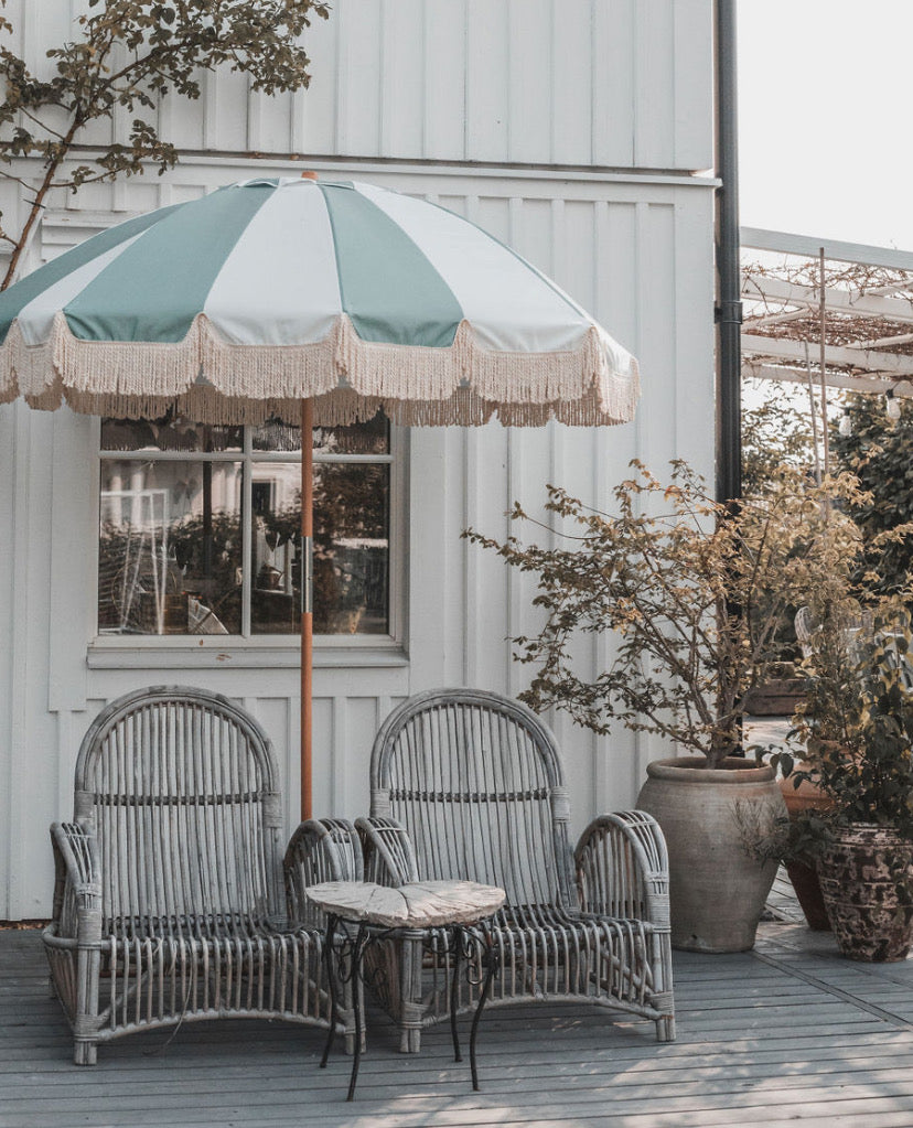 Rattan chairs with a striped fringed parasol on a wooden deck.