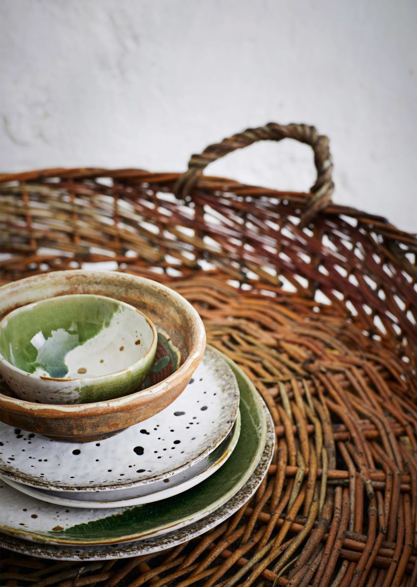 Rustic wicker handled tray with stack of handpainted plates and bowls
